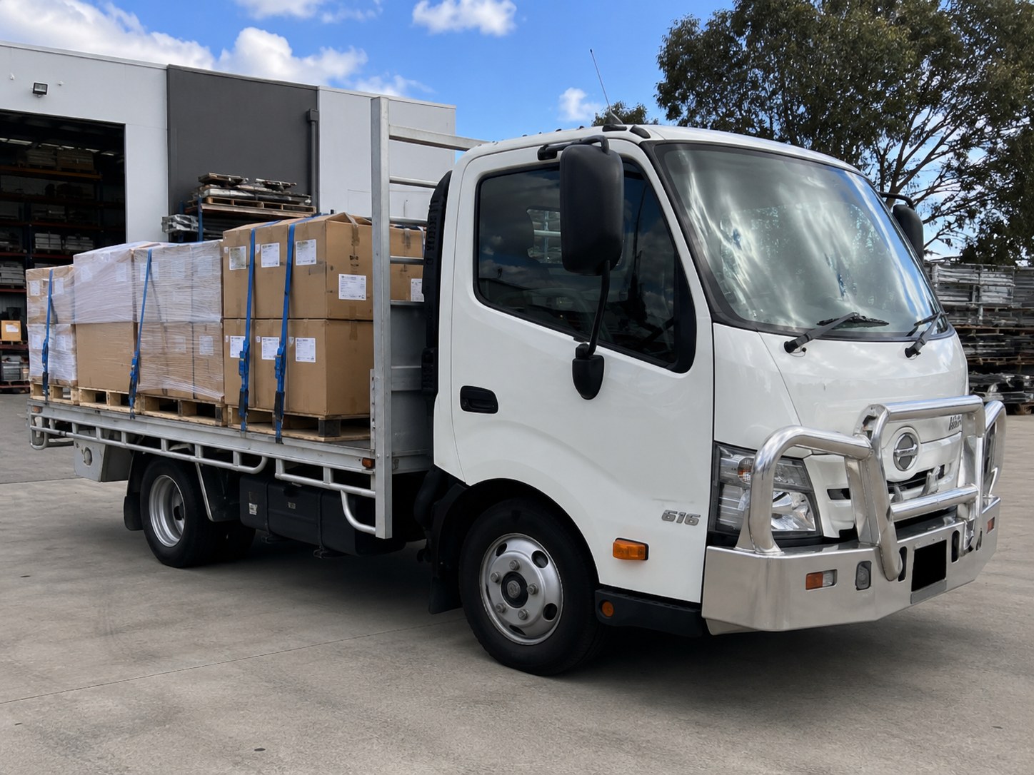 KDS Transport Hino flat-top tray truck loaded with strapped, palletised freight at a warehouse